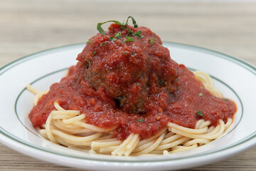 Hearty plate of spaghetti and an enormous meatball, Italian style, on a plate for a delicious dinner meal