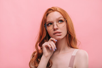 Close-up of fair-skinned young woman wearing glasses biting her lower lip looking up. Red-haired...