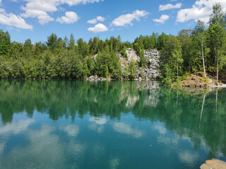 Fototapeta premium The shore of the lake Light with turquoise water, which reflects the trees and the sky with clouds, in the mountain park Ruskeala.