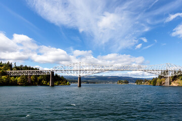 Panoramic wide view of the Bridge of the Gods, in Cascade Locks, Oregon, overlooking the Columbia River on a beautiful and breezy, wispy white cloud, blue sky afternoon.