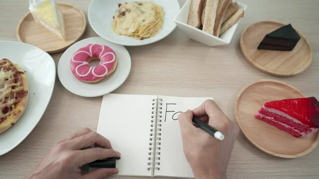 fat problem for diet. Man is losing weight and writes the word Fat on her notebook to remind him of weight loss. Fat foods or snacks cause obesity.