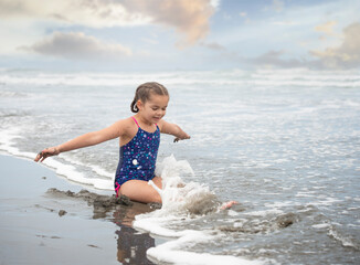 Mixed race girl sitting and playing in sand and waves of pacific ocean - 460403811