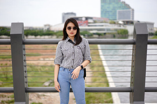 Young Beautiful Asian Woman Wearing Plaid Shirt And Blue Jeans Posing Outdoors