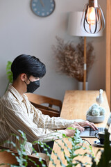 Young man wearing  protective mask working with laptop computer in coffee shop.