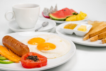 Traditional breakfast. Sausage and  scrambled eggs with tomato, green pepper and carrot on white plate and Toast with cup of tea, on white background