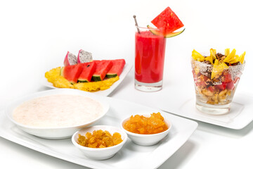 Breakfast. Bowl of porridge with raisins, and jam, glass of fresh exotic fruit exotic salad and sliced fruit, isolated on white.