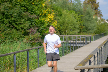 Senior man jogging across a footbridge over wetlands