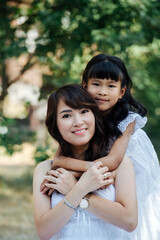 Cute portrait of a little girl hugging her mother from behind in a park