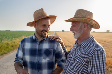 Senior farmer with hand on shoulder of young man talking smiling in field.