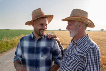 Senior farmer with hand on shoulder of young man talking smiling in field. © Budimir Jevtic
