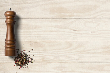 Pepper grinder with pepper on clean wooden background with space for text
