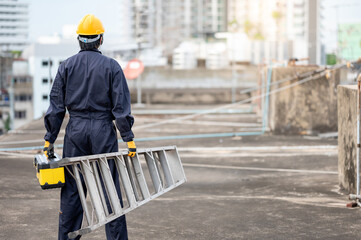 Asian maintenance worker man with protective suit and safety helmet carrying aluminium step ladder...