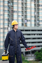 Asian maintenance worker man wearing protective suit and helmet holding red aluminium spirit level tool or bubble levels and work tool box at construction site. Equipment for civil engineering project