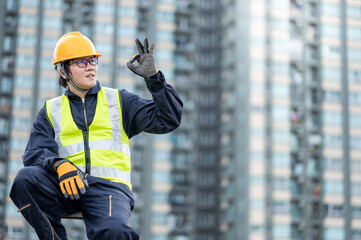 Asian maintenance worker man with safety helmet and green vest showing OK gesture hand signal at...