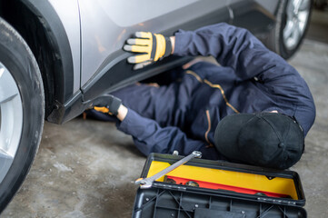 Asian auto mechanic working under car checking suspension system part in auto service garage....
