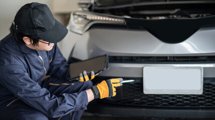 Asian auto mechanic holding digital tablet checking car engine and license plate in auto service garage. Mechanical maintenance engineer working in automotive industry. Automobile servicing and repair