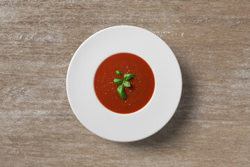 Tomato soup in white plate on wooden background