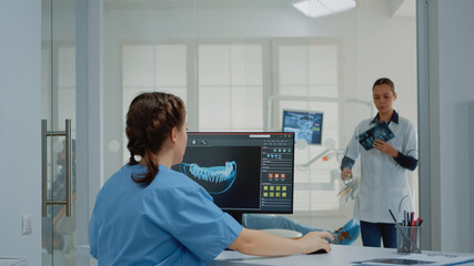 Dentistry assistant using computer with virtual teeth animation while giving x ray scan to dentist...