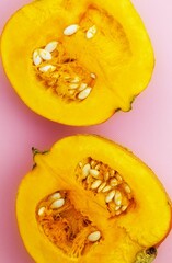 Two fresh pumpkin halves lie on a pink background