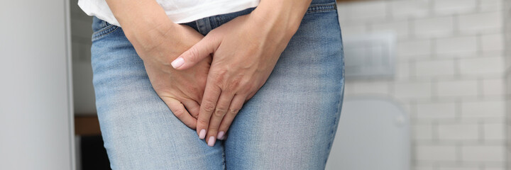 Woman stands in bathroom and covers her lower abdomen with her hand