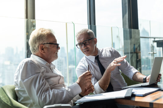 Picture of young business man taking to his older business partner. They are in white shirt and black tie. They are in a hotel lobby. 