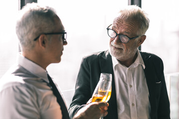 Picture of young business man taking to his older business partner. They are in white shirt and black tie. They are in a hotel lobby. 