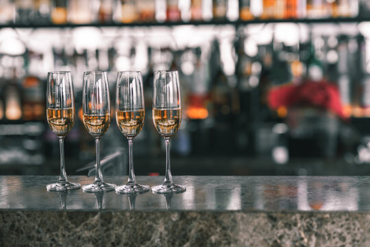 A picture of four glass of champagne placing on a bar. There are many bottle behind.