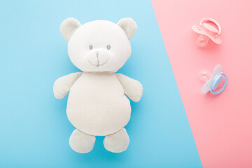 White teddy bear and two silicone soothers on light pink blue table background. Pastel color. Closeup. Baby things. Top down view.