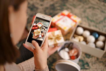 Flat lay of Woman s hands wrapping Christmas gift and taking pictures on the phone.