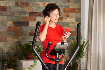 Fototapeta na wymiar Woman exercising at home on cross training elliptical using mobile phone