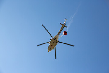 Helicopter going to fire area to extinguish forest fire.  Helicopter with a water bucket on a blue...