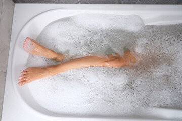 Women beautiful slender legs in bath with water and foam