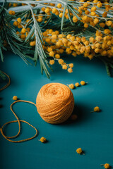 a skein of yellow sewing threads on a blue monochrome background with dried mimosa flowers in the background. the concept of needlework and leisure. side view