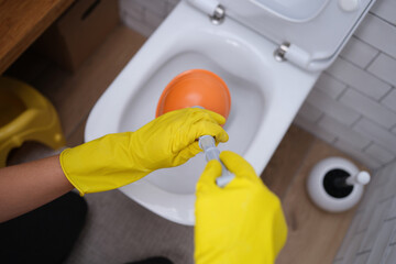 Person in yellow gloves and plunger cleans toilet closeup