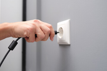 Woman hand inserts an electrical plug into outlet closeup - obrazy, fototapety, plakaty