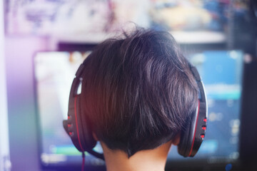 young boy wearing headphones playing games from behind.