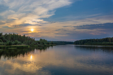 A picturesque landscape with a sunset sky reflected in a pond. Forest on the horizon. Sunset over the lake.