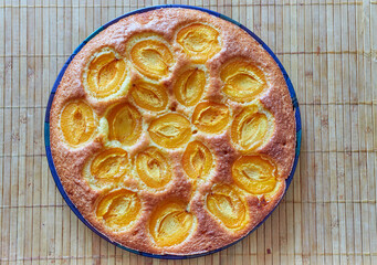 Sweet round pie with apricots on a wooden rustic table.