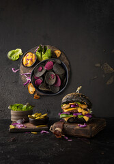 Black burger with cheese,mushrooms,beef cutlet,sauce,greenery and black crisps on dark background.Trend photo in two planes.