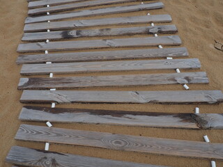Wooden footbridge on a sandy beach. Uneven, damp wooden planks held together. The edge of the beach...