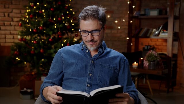 Older man reading book at home at Christmas in winter