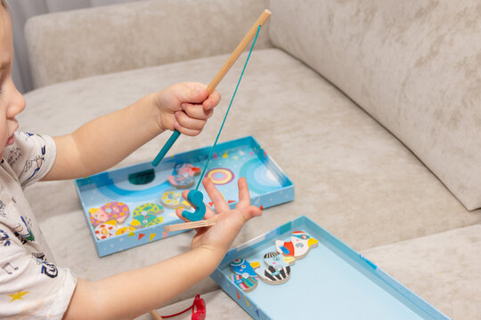 a little boy playing fisherman catches wooden fish in a box with a toy fishing rod with a magnet