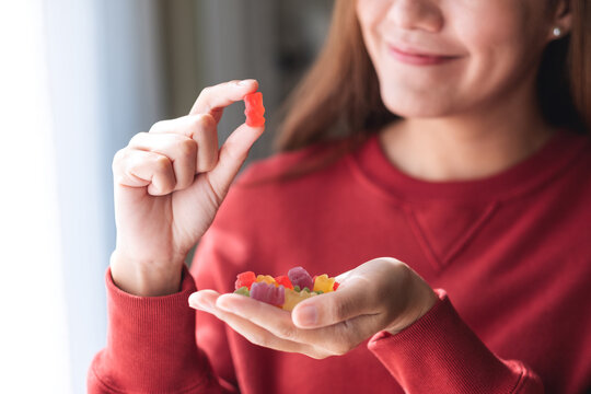 Closeup image of a young woman holding and looking at a red jelly gummy bear