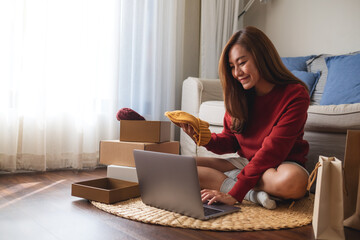 A woman using laptop for online shopping , opening shopping bags and postal parcel box at home