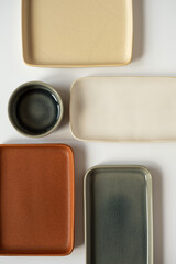 Empty blank ceramic round bowl and square plates on white background. Aesthetic minimal traditional handcrafted homemade kitchenware concept. Top view, flatlay