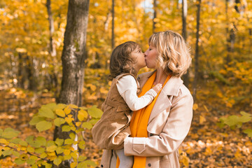 Fototapeta premium Woman with kid girl outdoors in fall. Child kissing mom. Mothers day holiday and autumn concept.