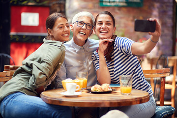two young adult females taking selfie on cell phone with elderly woman, sitting, smiling,