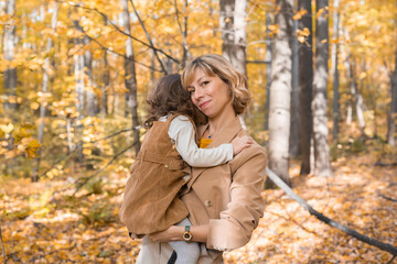 Mother with child in her arms against background of autumn nature. Family and season concept.
