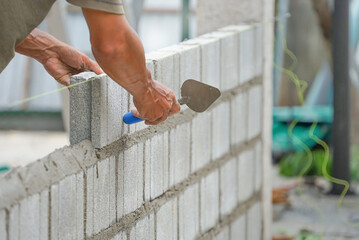 bricklayer hands hold  aluminium brick trowel installing brick blocks on construction site,...