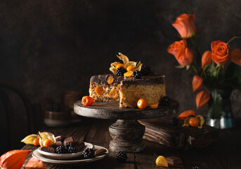 Delicious chocolate cake with physalis,blackberries,roses,vintage dishes on wooden background in rustic style.Still life with dessert in autumn colors.